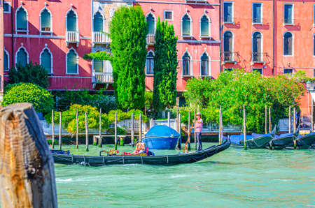 Venice, Italy, September 13, 2019: gondolier and tourists on gondola traditional boat sailing on water of Grand Canal waterway with Venetian architecture typical colorful buildings backgroundのeditorial素材