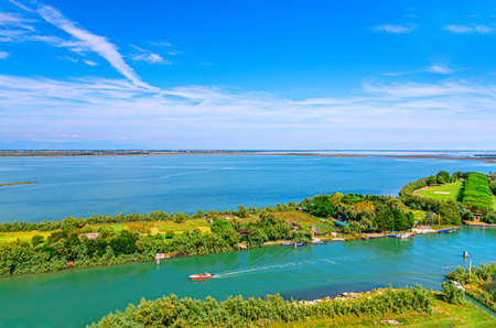 Aerial view of Torcello islands, water canal with fishing motor boats and green trees. Panoramic view of Venetian Lagoon from bell tower. Veneto Region, Northern Italy. Blue cloudy sky background.の写真素材