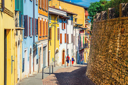 Typical narrow street in old historical center of Desenzano del Garda town with cobblestone road and traditional colorful buildings with shutter windows, Lombardy, Northern Italyの写真素材