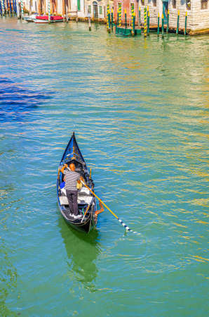 Gondolier on sailing gondola traditional boat in water of Grand Canal waterway in Venice historical city center with Venetian architecture colorful buildings around. Veneto Region, Northern Italy.の写真素材