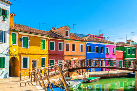 Colorful houses of Burano island. Multicolored buildings on fondamenta embankment of narrow water canal with fishing boats and wooden bridge, Venice Province, Veneto Region, Northern Italyの写真素材
