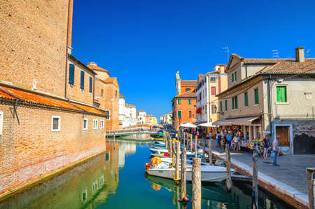 Chioggia, Italy, September 16, 2019: narrow water canal Vena with moored multicolored boats between old colorful buildings and brick bridge, blue sky background in summer day, Veneto Regionのeditorial素材