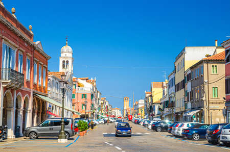 Chioggia, Italy, September 16, 2019: row of colorful multicolored buildings, riding cars and walking people on main street in historical town center, blue sky background in summer day, Veneto Regionのeditorial素材