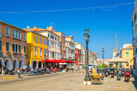 Chioggia, Italy, September 16, 2019: row of colorful multicolored buildings, parking bikes and scooters on main street in historical town center, blue sky background in summer day, Veneto Regionのeditorial素材