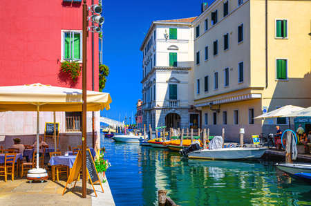 Chioggia, Italy, September 16, 2019: Vena water canal with colorful boats moored near embankment and old buildings in historical center of Chioggia town in summer day, Veneto Regionのeditorial素材