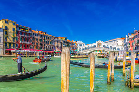 Venice, Italy, September 13, 2019: gondolier and tourists on gondola traditional boat sailing on water of Grand Canal with Venetian architecture typical colorful buildings and Rialto Bridge backgroundのeditorial素材