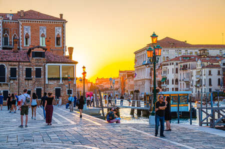 Venice, Italy, September 13, 2019: people tourists walking down fondamenta Salute embankment promenade near pier of Grand Canal waterway at sunset, Veneto Region, Northern Italy. View against sunのeditorial素材