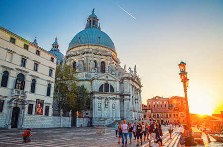 Venice, Italy, September 13, 2019: people tourists walking down fondamenta embankment near Basilica di Santa Maria della Salute Catholic church on Punta della Dogana on and pier of Grand Canal, Italyのeditorial素材