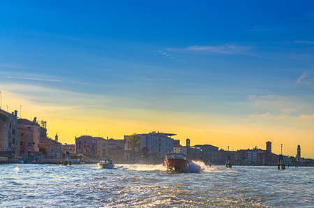 Yacht boats racing sailing on water of Venetian lagoon between wooden poles. Venice city coast with buildings background, Veneto region, Northern Italyの写真素材