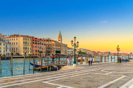 Venice evening view with Fondamenta Salute embankment promenade near pier of Grand Canal waterway at sunset, Campanile bell tower and row of baroque style buildings in San Marco sestiere, Italyの写真素材