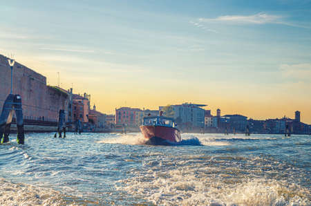 Venice, Italy, September 14, 2019: Yachtman driving yacht boat racing sailing on water of Venetian lagoon between wooden poles. Venice city coast with buildings background, Veneto regionのeditorial素材