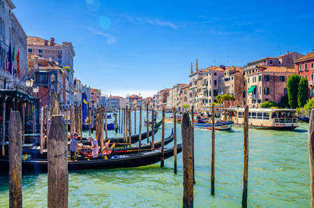 Venice, Italy, September 13, 2019: gondolier on moored gondola traditional boat on water of Grand Canal waterway in wooden pier dock, typical colorful buildings and sailing boats backgroundのeditorial素材