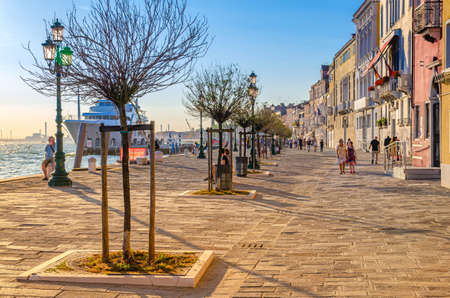Venice, Italy, September 13, 2019: people tourists are walking down embankment promenade Fondamenta Zattere Al Ponte Lungo with trees and yacht moored in water of Giudecca canal waterfrontのeditorial素材