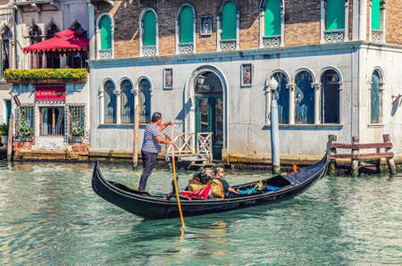 Venice, Italy, September 13, 2019: gondolier and tourists on gondola traditional boat sailing on water of Grand Canal waterway with Venetian architecture typical colorful buildings backgroundのeditorial素材