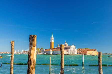 San Giorgio Maggiore island with Campanile San Giorgio in Venetian Lagoon, wooden poles in water of San Marco basin waterway foreground, blue clear sky, Veneto Region, Italy, Venice cityscapeの写真素材