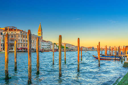 Venice evening view with wooden poles and boats near pier of Grand Canal waterway at sunset, Campanile bell tower and row of baroque style buildings in San Marco sestiere, Veneto region, Italyの写真素材