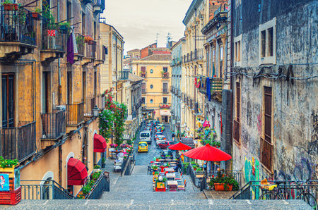 Italy, Catania, May 12, 2018: Narrow street with stairs, old buildings with balconies and street restaurants with tents and umbrellas in Catania historical city center of Sicily islandのeditorial素材