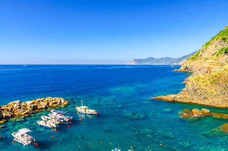Fishing boats moored on water in harbor of Ligurian and Mediterranean Sea near coastline of Riviera di Levante of National park Cinque Terre Coast with blue sky, Riomaggiore village, Liguria, Italyの写真素材