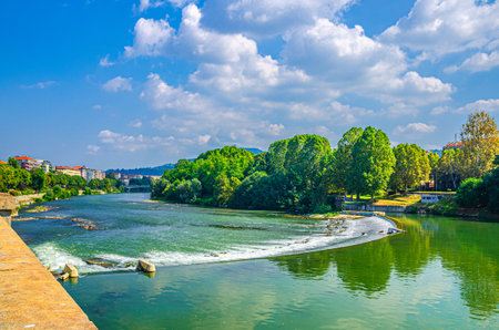 Po river in Turin city historical center with water dam and green trees on shore, blue sky white clouds background, Piedmont, Northern Italyの写真素材