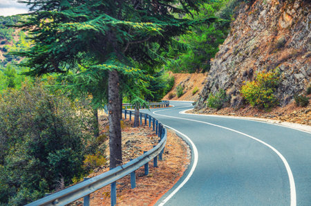 Asphalt serpentine road in Troodos mountain range with roadside fence and trees, Cyprus
