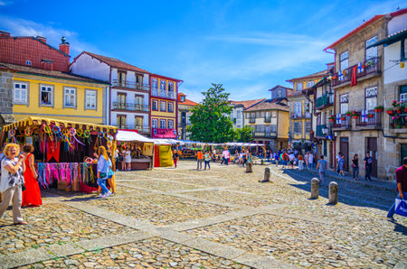 Guimaraes, Portugal, June 24, 2017: people tourists walking down cobblestone square with traditional...