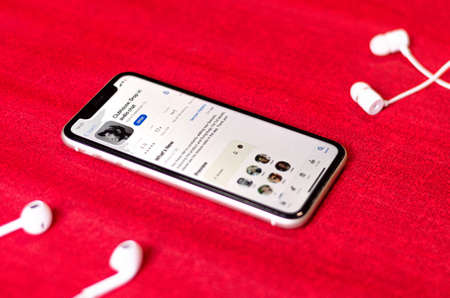 Minsk, Belarus, March 2, 2021: Clubhouse drop-in audio chat application view on smartphone screen and two wired earphones on red background on sides, social network audio chat app on Apple App Storeのeditorial素材