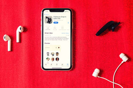 Minsk, Belarus, March 2, 2021: Clubhouse drop-in audio chat application view on smartphone screen and various types of earphones and earbuds on red background on sides, social app on Apple App Storeのeditorial素材
