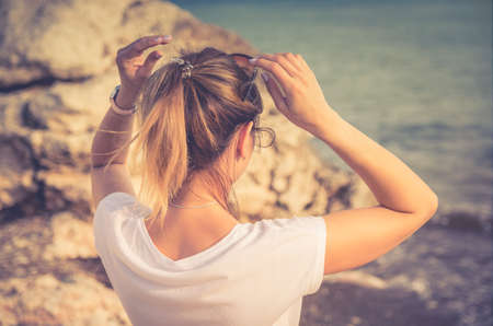 Young woman traveler with white shirt and ponytail stay at beach in Aphrodite bay with stone rocks,...
