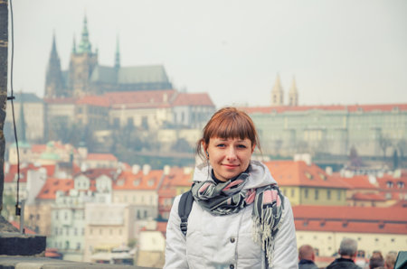 Close-up portrait of young caucasian girl tourist looking at camera and smile, Prague Castle and St. Vitus Cathedral in Prague city historical center background, woman on vacation in Czech Republicの写真素材