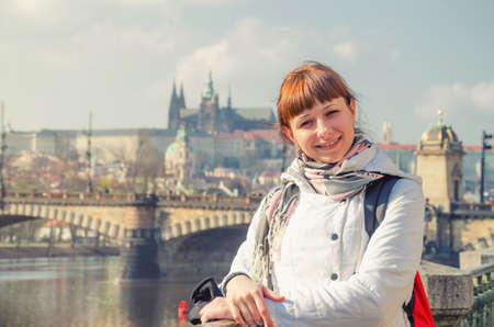 Close-up portrait of young girl tourist looking at camera and smile, Charles Bridge Karluv Most across Vltava river, Prague Castle and St. Vitus Cathedral in Prague city historical center backgroundの写真素材