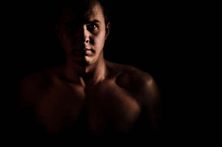 Close-up portrait of young muscular shirtless nake male bodybuilder man with athletic body looking at camera and posing, low key portraitの写真素材
