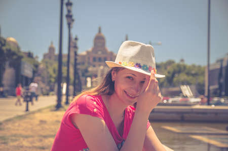 Young beautiful woman traveler with red dress and hat posing in Barcelona city in sunny summer day, Palau Nacional National Palace of Montjuic and National Art Museum of Catalonia blurred backgroundの写真素材