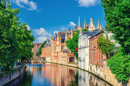 Groenerei Green Canal water of Reie river with stone bridge, green trees on embankment in Brugge old town quarter district, houses buildings in Bruges city historical centre, Flemish Region, Belgiumの写真素材