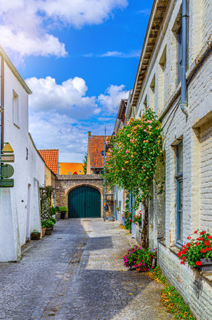 Empty narrow cobblestone dead end quiet street, buildings with flowers on brick walls in Brugge city historic center, Bruges old town quarter district, West Flanders province, Flemish Region, Belgiumの写真素材