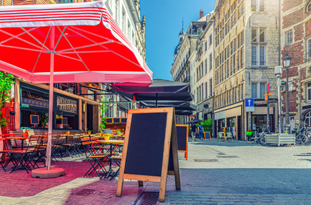 Street restaurant with tables and chairs on narrow street, road with paving stone, old buildings in Antwerp historical city center, street cafe in old town Antwerpen, Belgiumの写真素材