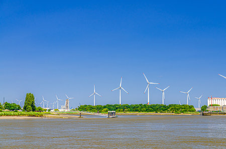 Landscape of Scheldt river and Linkeroever Left bank of Antwerp with Windmill farm wind power plant turbines on horizon, Antwerpen port area, Flemish Region, Belgiumの写真素材