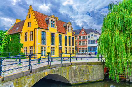Old houses on embankment of Lieve water canal, trees on bank, Lievebrug bridge in Ghent historical city center Prinsenhof Princes Court quarter district, Gent old town, Flemish Region, Belgiumの写真素材