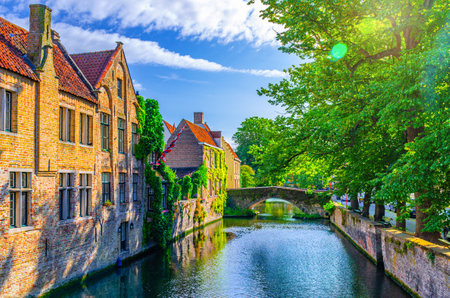 Meebrug stone bridge across Groenerei Green Canal water, embankment of Reie river with trees and plants in Brugge old town, medieval buildings in Bruges city historic centre, Flemish Region, Belgiumの写真素材