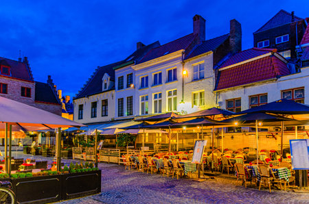 Street restaurant with tables and chairs on Huidenvettersplein Tanners Square in Brugge old town quarter district, Bruges city historical centre, evening dusk twilight view, Flemish Region, Belgiumの写真素材