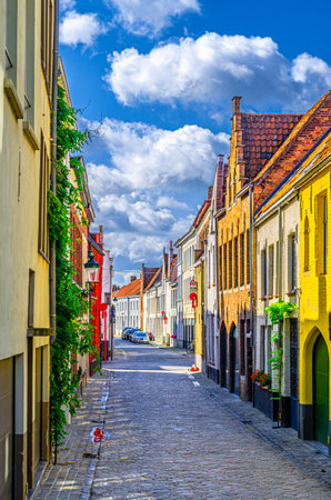 Bruges cityscape with empty narrow cobblestone street, colorful buildings in Brugge city historical center, Bruges old town Sint-Anna quarter medieval district, vertical view, Flemish Region, Belgiumの写真素材