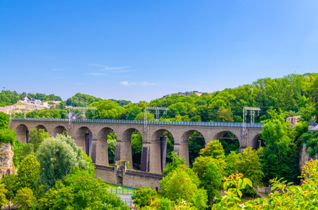 Pulvermuhl Viaduct Biisser Breck railway stone arch bridge across Alzette valley and Maierchen stone defensive wall in Luxembourg City historical centre, park with green trees and blue sky backgroundの写真素材