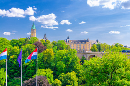 Luxembourg City historical center with Luxembourg and EU flags on poles, Pont Adolphe Bridge, Petrusse Parks green trees and State Bank and Savings Bank on Fort Bourbon squareの写真素材