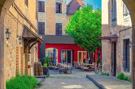 Typical small courtyard with tables and chairs near old medieval houses buildings and green tree, typical French courtyard in Dijon city historical centre, Bourgogne-Franche-Comte region, Franceの写真素材