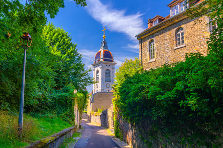 Narrow street with stone fence and green plants, street lamp and La CathÃ©drale Saint-Jean Cathedral tower in Besancon old town center ville, La boucle de BesanÃ§on city historic centre, Franceの写真素材