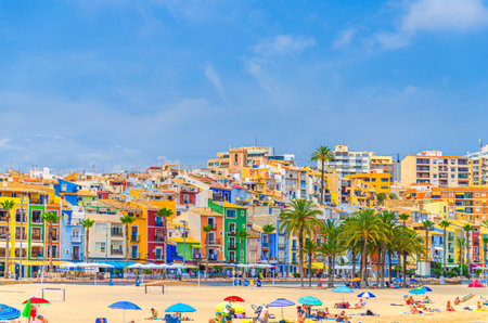 Villajoyosa, Spain, June 5, 2025: people relaxing on sandy beach on Costa Blanca coast of Villajoyosa town, tourists on Platja Center La Vila Joiosa city with colorful houses in sunny summer dayのeditorial素材