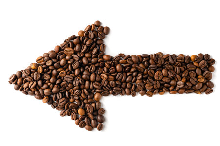 Unique arrow sign made of dark coffee beans pointing left on white background for navigation or...