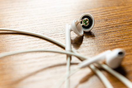 Minimalist composition of white electronic earbuds and thin wires on a natural wood texture for...