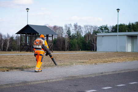 Maintenance staff member in protective clothing performing routine cleaning tasks on a public road...