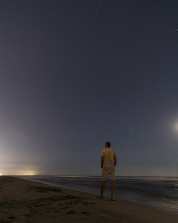 A person stands on a beach at night, gazing at a starry sky.の写真素材