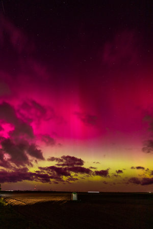 Vibrant aurora borealis with pink and yellow hues over a rural landscape.の写真素材